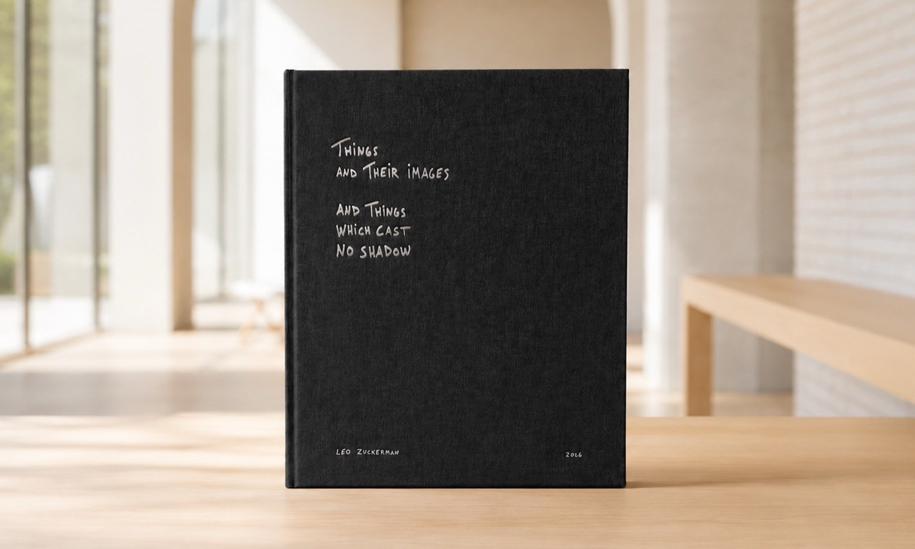 Things and Their Images, a black linen hardcover book with a handwritten title, on a pale wooden table